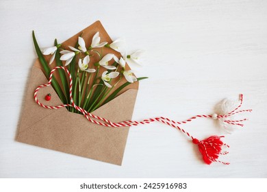 Envelope with spring flowers snowdrops and red and white martenitsa, tassel cord, a symbol of the Martisor holiday, Baba Marta on a white wooden background. Greeting card. - Powered by Shutterstock