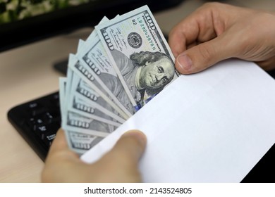 Envelope with US dollars in male hands. Man pulls money out of an envelope on PC keyboard background, wages, bonus or bribe concept