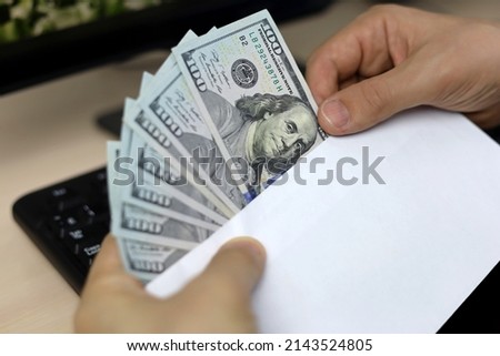 Envelope with US dollars in male hands. Man pulls money out of an envelope on PC keyboard background, wages, bonus or bribe concept