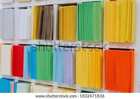 Envelopes stacks sorted on a shelf by color. Colorful mail wraps arranged in categories.