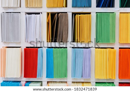 Envelopes stacks sorted on a shelf by color. Colorful mail wraps arranged in categories.