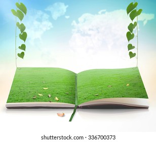 Environment Day Concept: Open Magic Book In Green Meadow With Heart Shape Of Leaves Over Blurred World Map Of Cloud Background