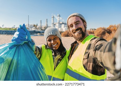 A environmental activist or volunteer multiracial couple picking up trash og the beatch, and taking a selfie portrait smiling looking at camera showing a recycle plastic bag. High quality photo - Powered by Shutterstock