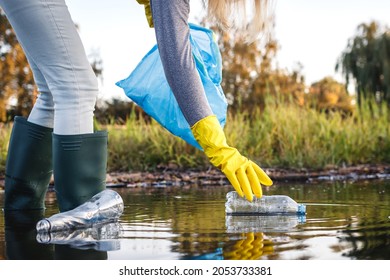 Environmental cleanup. Volunteer picking up plastic bottle from polluted river or lake. Water pollution with plastic garbage - Shutterstock ID 2053733381