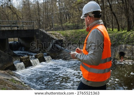 Environmental engineer inspecting a river dam and water level control system for ecological monitoring. Ecologist hydrologist working near a weir for flood prevention and environmental protection.