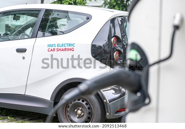 Environmental friendly electric battery powered\
white sedan car sharing vehicle parked outdoor connected to\
charging station