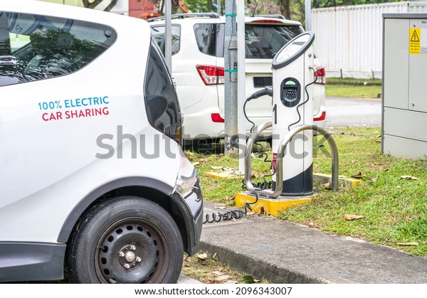 Environmental friendly electric battery powered
white sedan car sharing vehicle parked outdoor connected to
charging station