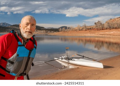 environmental portrait of a senior man wearing drysuit and life jacket with a rowing shell on lake shore - Powered by Shutterstock