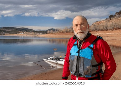 environmental portrait of a senior man wearing drysuit and life jacket with a rowing shell on lake shore - Powered by Shutterstock