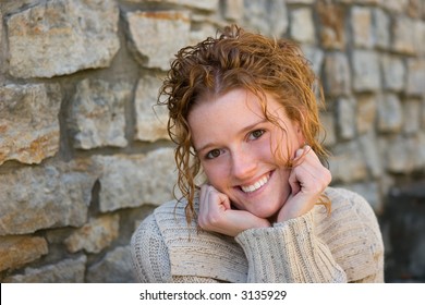 Environmental Senior Portrait of redhead female high school student with stone wall in background.