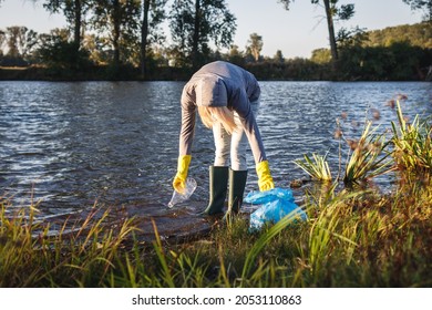 Environmental Volunteer Cleaning River From Plastic Garbage. Water Pollution. Woman Picking Up Plastic Bottle From Riverbank