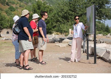 EPHESUS, TURKEY - JUNE 6, 2014: A group of tourists gather around a tour guide in the celsus library area of Ephesus in order to hear the guide tell them about the site.