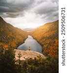 Epic Autumn Indian Head Adirondacks Viewpoint Female Hiker Yellow Jacket Stands in Sun Rays on Mountain. Colorful Fall Foliage and Lake Powerful Scene