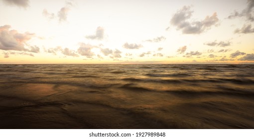 Epic colorful glowing golden sunset clouds above the sea after a thunderstorm. Dramatic sky. Waves and water splashes texture. Idyllic seascape. Concept image, long exposure. Picturesque scenery