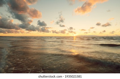 Epic colorful glowing golden sunset clouds above the sea after a thunderstorm. Dramatic sky. Waves and water splashes texture. Idyllic seascape. Concept image, long exposure. Picturesque scenery