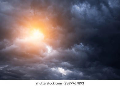 Epic dramatic storm sky with sun. Dark grey blue cumulus rain clouds with orange yellow light and sunlight, thunderstorm