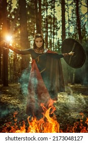 Epic Fantasy. Divine Female Warrior Valkyrie Fights With A Sword And Shield In Her Hands In The Forest Engulfed In Smoke And Fire. Scandinavian Mythology.