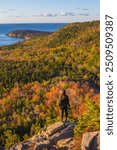 Epic Female Hiker Black Shirt Stands on Rock Edge in Acadia National Park Sunrise Beehive Trail Wide Landscape During Fall Foliage in Maine Bright Sun