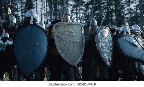 Epic Invading Army Of Medieval Knights On Battlefield, Plate Body Armored Soldiers Hit Shields With Swords In Battle Cry. War And Conquest. Historical Reenactment.