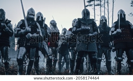 Epic Invading Army of Medieval Knights on Battlefield. Armored Soldiers in Helmets, With Shields and Swords ready for the Battle. War, Conquest, Crusade. Historical Reenactment.