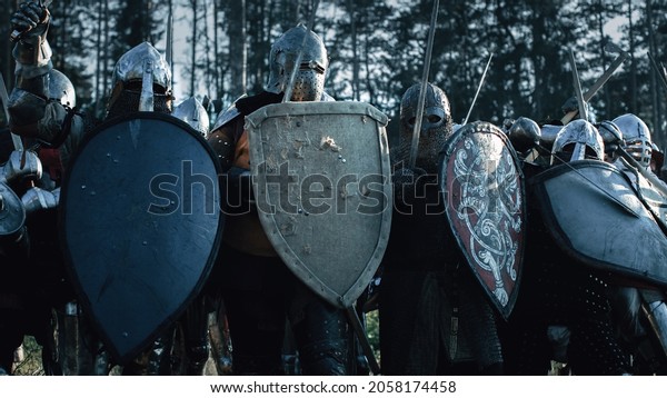 Epic Invading Army of\
Medieval Knights on Battlefield, Plate Body Armored Soldiers Hit\
Shields with Swords in Battle Cry. War and Conquest. Historical\
Reenactment.
