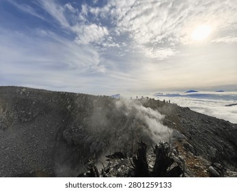 Epic panoramic view from an active volcanic peak with white sulfur steam rising from the crater rim, silhouetted hikers on the ridge, and a vast sea of clouds under a bright sun.
