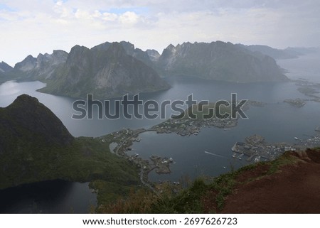 Epic panoramic view of dramatic mountains, deep fjords and coastal fishing village in northern Norway. Scenic landscape with steep peaks, calm water and traditional Nordic houses in summer. Travel and