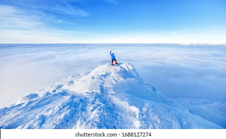 Epic scene of man at the summit of mountain as symbol of life success. Silhouette of man tourist standing at top. Incredible panoramic view of snow capped mountain ridge , horizon view over clouds. 