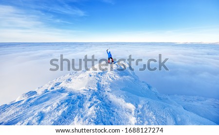 Epic scene of man at the summit of mountain as symbol of life success. Silhouette of man tourist standing at top. Incredible panoramic view of snow capped mountain ridge , horizon view over clouds. 