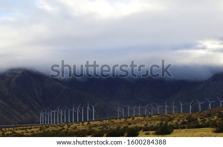An epic shot of a massive storm coming over the mountains, with some windmills beneath the clouds.