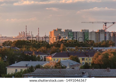 Epic storm clouds moving at sunset over city skyline. Oil refinery lights, power plant pipes with smoke. Constraction site with big crane