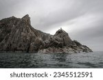 Epic summer arctic landscape. Coast of the Bering Strait. A sea hunter is standing on a high rock, waiting for the appearance of walruses and seals. Chukotka Peninsula, Far East of Russia. Overcast.