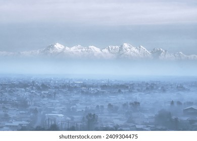 Epic view of a winter city shrouded in smog with majestic snowy mountains in the background. - Powered by Shutterstock