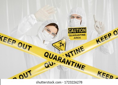 Epidemiologists A Man And A Woman In Protective Clothing Are In A Restricted Area With A Danger Sign. Yellow Line Keep Out Quarantine. Quarantine Alert Sign. Coronavirus, Covid-19.