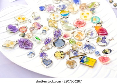 Epoxy Resin Jewelry - Many Handmade Pendants With Real Flowers And Plants Inside On White Stand. Making Exclusive Jewellery At Home