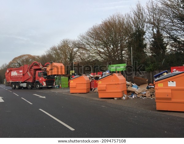 EPSOM, SURREY, UK\
- CIRCA 2021 DECEMBER: A red garbage truck at a recycling center\
has lifted an orange metal bin and is in the process of emptying\
its recycling waste