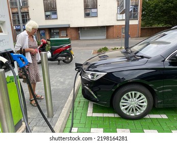 EPSOM, UK - CIRCA SEPTEMBER 2022: A Caucasian Female Looking At A Car Being Charged By A Rapid Charger.