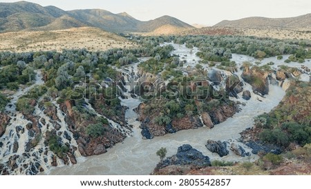 Epupa Falls presenting multiple cascading waterfalls and the winding Kunene River. Surrounded by lush vegetation and arid mountains