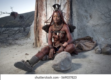 EPUPA, NAMIBIA CIRCA JUNE 2016 - A Himba woman poses for photographs in her village. Posing for photographs allows the Himba to live a traditional life in a modernising world.