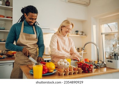 Equality concept. A happy interracial couple is preparing a meal and washing dishes at home together. The wife and husband are doing chores and cooking a meal together in the kitchen at home. - Powered by Shutterstock