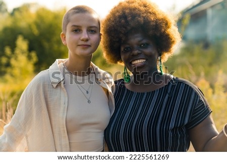 Equality in human relationships. Beautiful bond between two homosexual queer people - Black positive feminine woman with afro hairstyle and bald Caucasian skinny non-binary person. Outdoor shot with