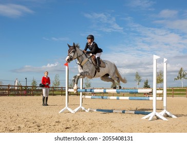 An Equestrian Athlete Jumps On A Horse Over A Barrier. There Is A Coach On The Field. Preparation Of An Athlete Before Competitions. Image With Selective Focus, Noise Effect, Toning