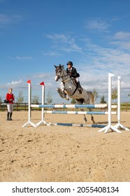 An Equestrian Athlete Jumps On A Horse Over A Barrier. There Is A Coach On The Field. Preparation Of An Athlete Before Competitions. Image With Selective Focus, Noise Effect, Toning