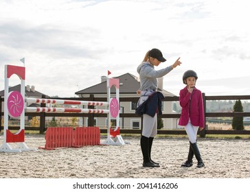 An Equestrian Coach Talks To A Child Equestrian Athlete. The Girl Is Dressed In Competition Equipment, A Jacket, White Breeches, Leather Boots And A Protective Helmet. Image With Selective Focus And N