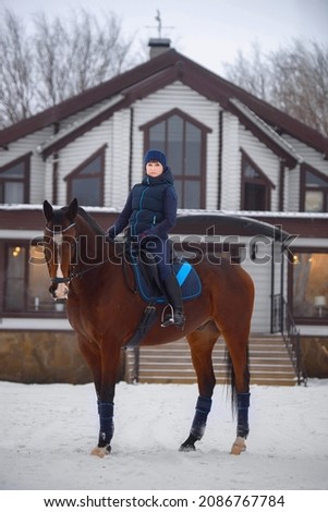 Equestrian country girl riding her horse in winter. A girl in a special riding uniform poses sitting in the saddle on her horse.
