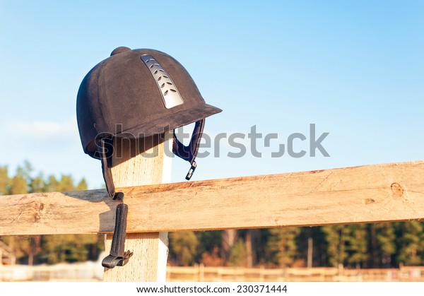 Equestrian equipment -\
helmet  hanging on the wooden fence with blue sky background.\
Outdoors close-up.