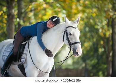 Reitfrau reitet auf dem Pferd und umarmt den weißen Reithals. Lebhaftes, im Freien gefärbtes Herbstbild mit Filter
