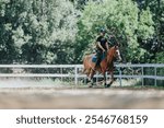 Equestrian rider training a horse in an outdoor setting, surrounded by trees and a white fence.