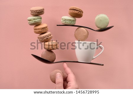 Equilibrium concept flat lay on coral color paper. Balancing cup of coffee and macarons on a finger