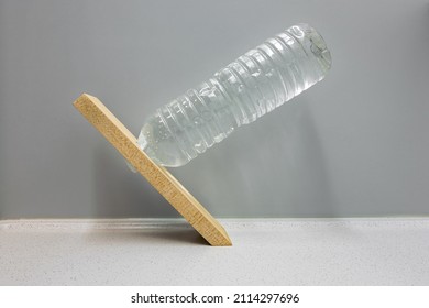 Equilibrium situation where a horizontal bottle filled with water appears to fall but is in perfect balance because the center of gravity is above the fulcrum. Optical illusion, used in physics class.
